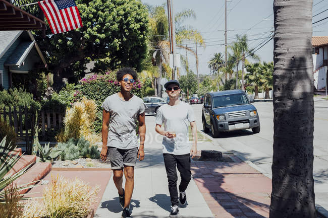 Amigos caminando por la calle soleada, Long Beach, California, EE.UU. - foto de stock