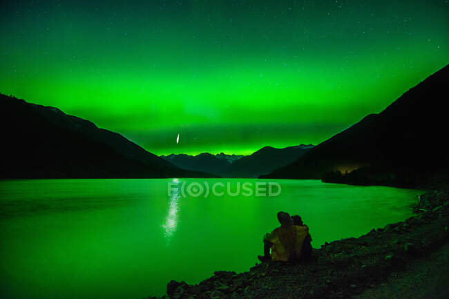 Couple sitting beside Lillooet Lake, watching northern lights, Pemberton, British Columbia, Canada — Stock Photo
