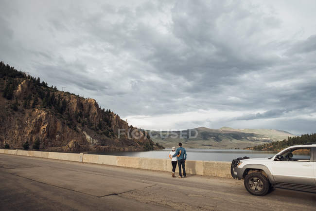 Pareja de pie en la carretera junto Dillon embalse, mirando a la vista, Silverthorne, Colorado, EE.UU. - foto de stock