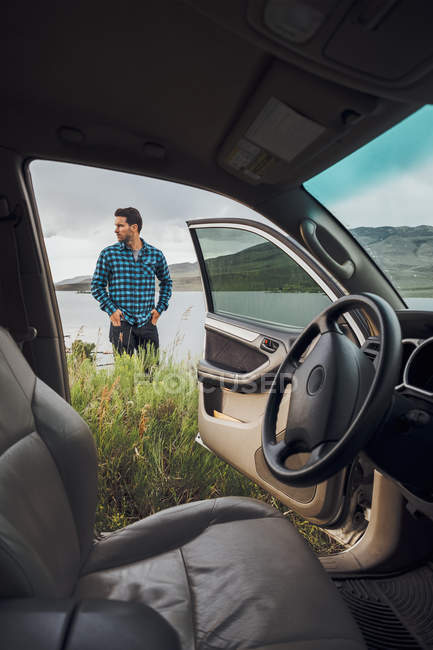 Mid adult man standing beside Dillon Reservoir, view through parked car, Silverthorne, Colorado, USA — Stock Photo