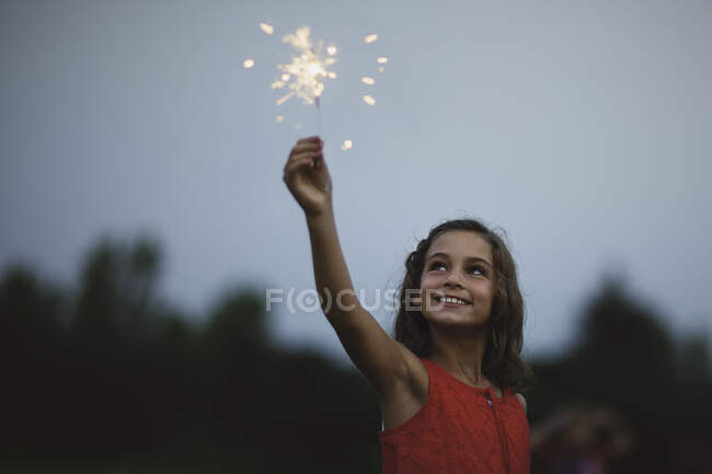 Chica con brazo levantado celebración sparkler - foto de stock