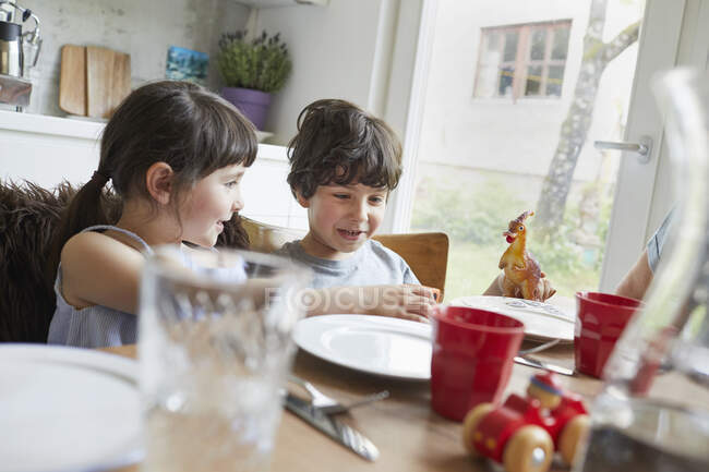 Niño y niña sentados en la mesa, sonriendo - foto de stock