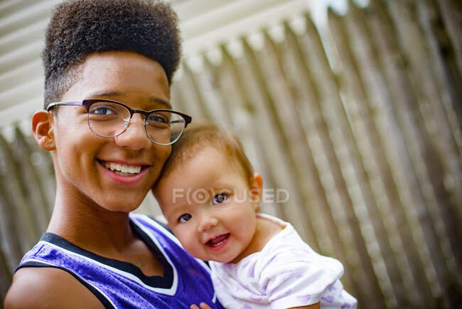 Portrait of teenage boy carrying baby girl in arms — Stock Photo