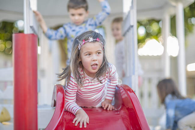 Mädchen im Kindergarten liegt auf Spielplatz-Rutsche im Garten — Stockfoto