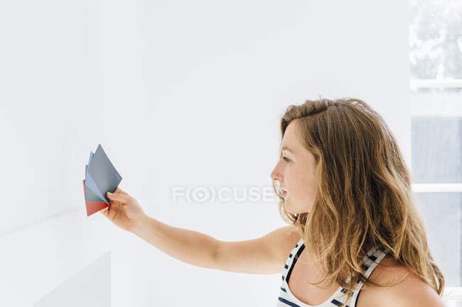 Young woman holding paint swatches against wall — Stock Photo