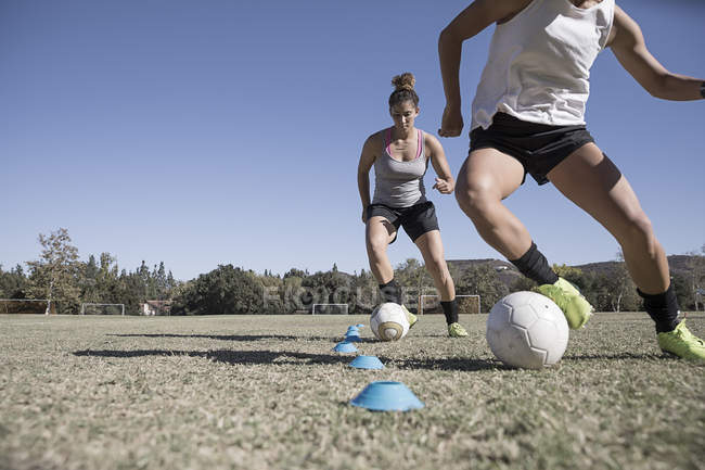 Two young women dribbling footballs on soccer pitch — Stock Photo