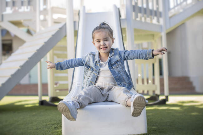 Menina na pré-escola, retrato sentado no playground slide no jardim — Fotografia de Stock