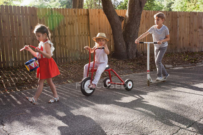 Tres niños en mini desfile, golpeando tambor, montando triciclo y usando scooter - foto de stock