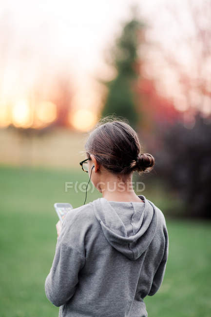 Vista trasera de la chica con auriculares y smartphone en el jardín - foto de stock