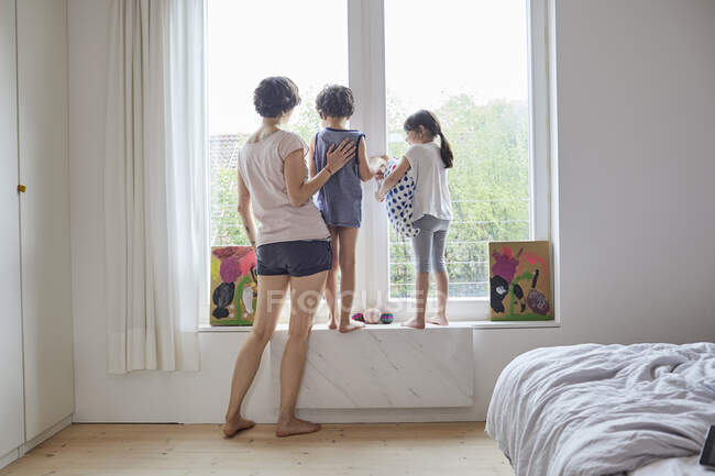Madre, figlio e figlia guardando fuori dalla finestra della camera da letto, vista posteriore — Foto stock