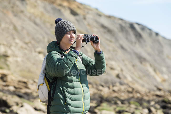 Woman using binoculars on rocky coast — Stock Photo