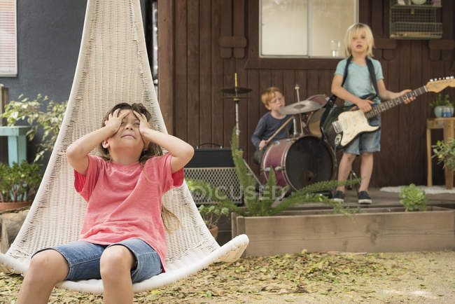 Girl holding hands on head and boys playing on musical instruments — Stock Photo
