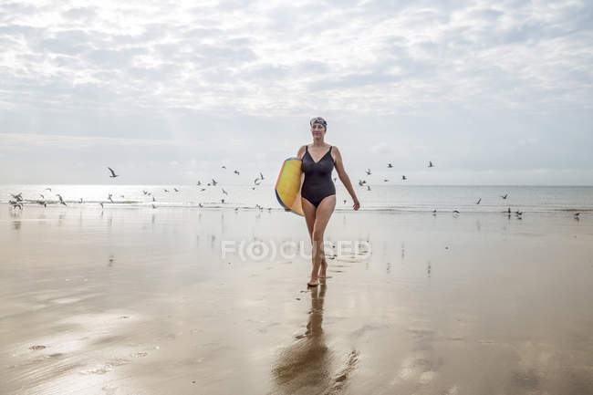 Mature woman carrying surfboard on beach — Stock Photo