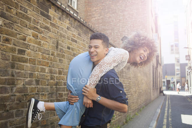 Pareja joven jugando en la calle, hombre llevando a la mujer por encima del hombro - foto de stock