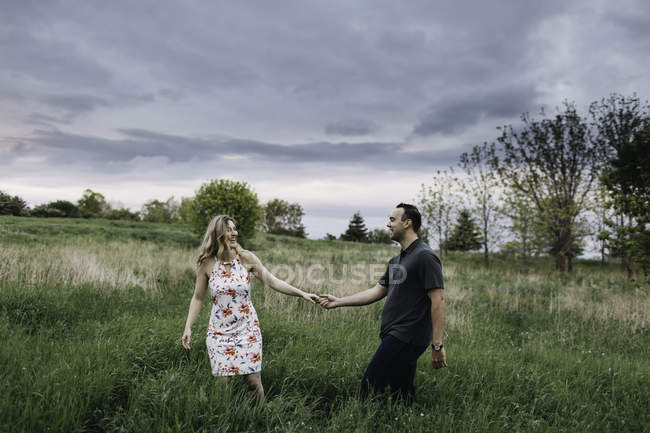 Романтическая пара, держащаяся за руки в поле — стоковое фото