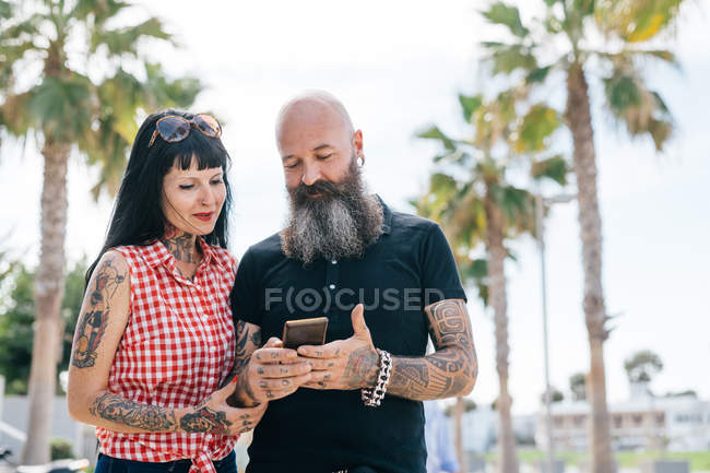 Зрелая пара хипстеров в парке смотрит на смартфон, Валенсия, Испания — стоковое фото