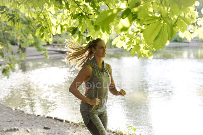 Young female running by lake in park — Stock Photo