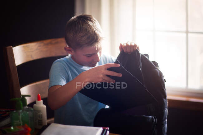 Мальчик упаковывает рюкзак со школьными принадлежностями — стоковое фото
