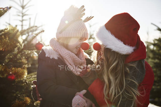 Chica y madre en el bosque de árboles de Navidad con narices rojas - foto de stock
