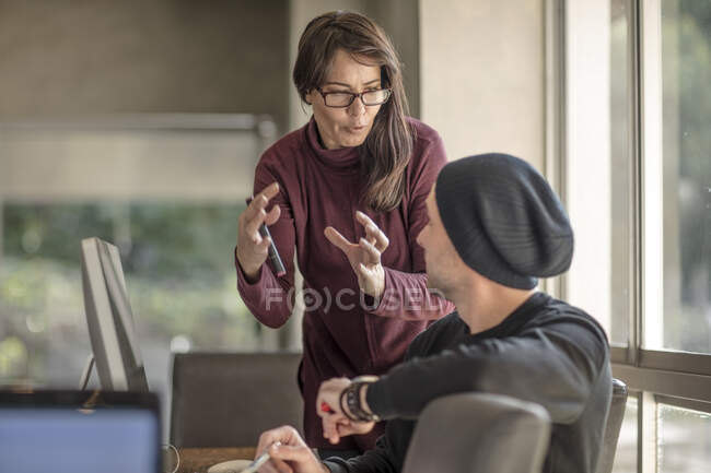 Mujer de negocios explicando a joven diseñador masculino en el escritorio del hogar - foto de stock