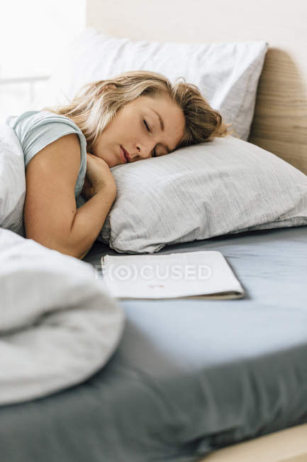 Jeune femme endormie avec magazine au lit — Photo de stock