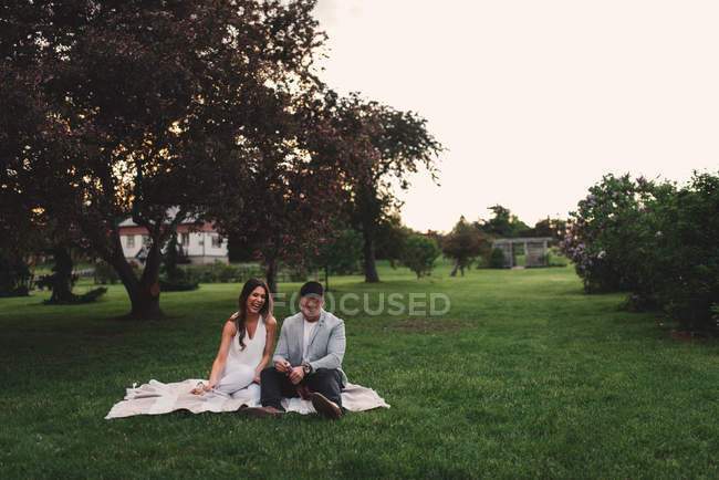 Romantic young couple opening pink champagne in park at dusk — Stock Photo
