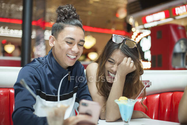 Молода пара сидить в їдальні, дивлячись на смартфон, сміється — стокове фото