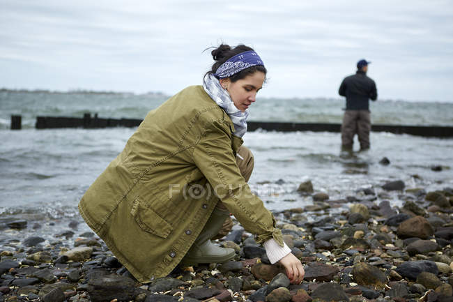 Mujer joven agachándose en la playa mientras que la pesca novio - foto de stock