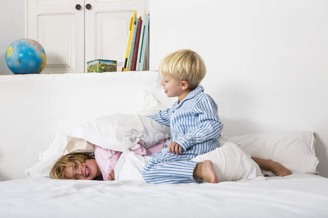 Niño y mujer gemelo jugar luchando en la cama - foto de stock