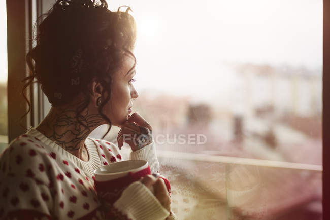 Giovane donna dalla finestra che tiene bevanda calda — Foto stock