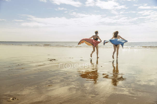 Madre e hija corriendo en la playa con chales en el aire - foto de stock