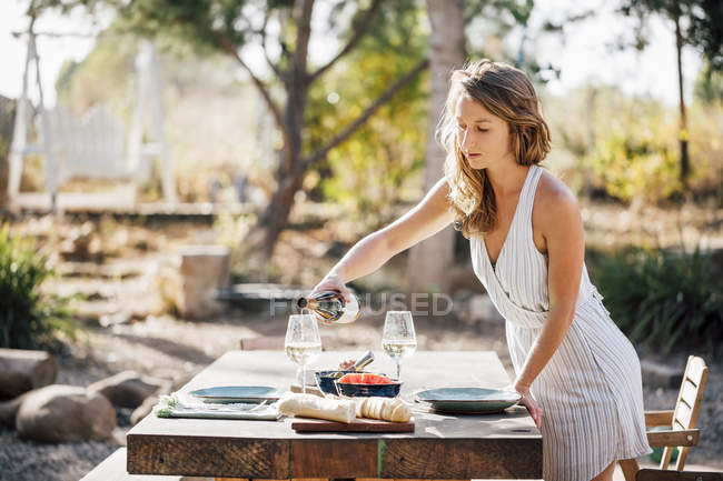 Jeune femme versant du vin et préparant la table à manger — Photo de stock