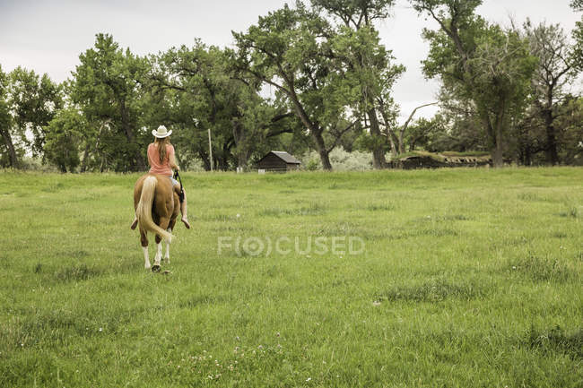 Rückansicht einer jungen Frau, die barfuß auf einem Pferd auf einem Ranchfeld reitet, Bridger, Montana, USA — Stockfoto