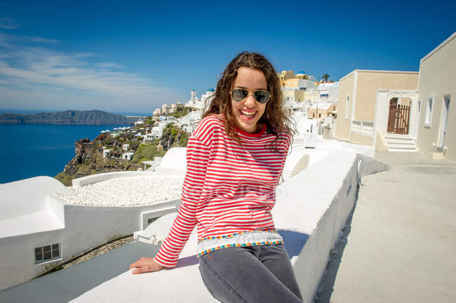 Ragazza rilassante sul muro e sorridente alla macchina fotografica, Santorini, Kikladhes, Grecia — Foto stock