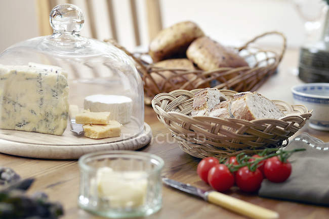 Table with fresh bread, cheeses and vine tomatoes — Stock Photo