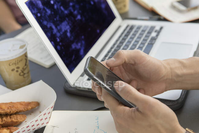 Hand eines Geschäftsmannes hält Smartphone am Cafétisch — Stockfoto