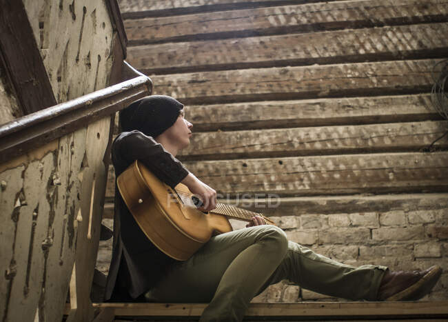 Молодой человек сидит на лестнице, играет на гитаре — стоковое фото