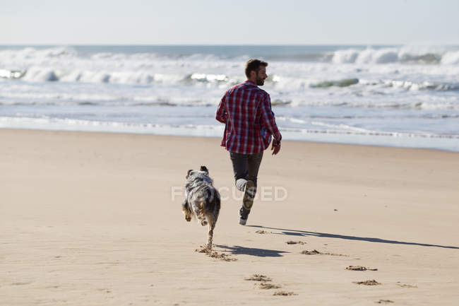 Homme courant avec chien sur une plage de sable — Photo de stock