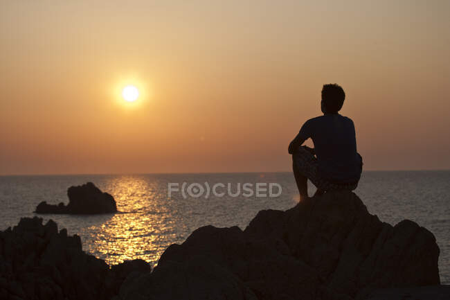 Silhueta de homem sobre rochas olhando para longe ao pôr do sol sobre o mar, Olbia, Sardenha, Itália — Fotografia de Stock