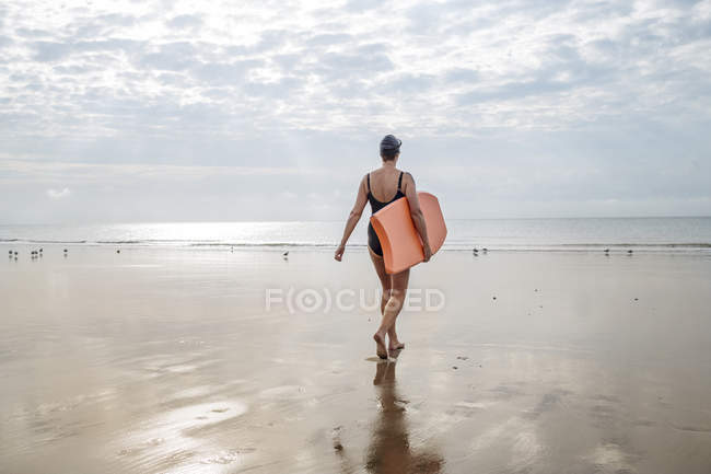 Visão traseira da mulher andando com prancha na praia — Fotografia de Stock