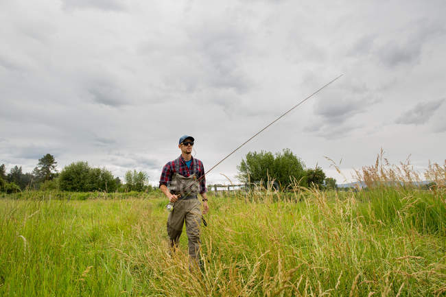 Pescador con caña de pescar caminando en el campo de hierba, Clark Fork, Montana - foto de stock