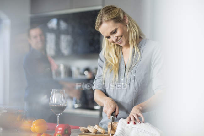 Mulher cortando pão no balcão da cozinha — Fotografia de Stock
