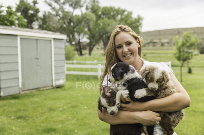 Ritratto di giovane donna con tre cuccioli in braccio in ranch, Bridger, Montana, USA — Foto stock