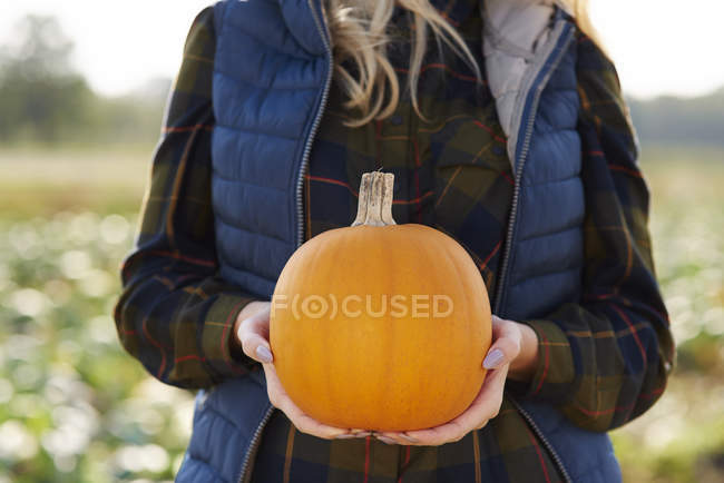 Mid section of woman holding pumpkin in pumpkin patch field — Stock Photo