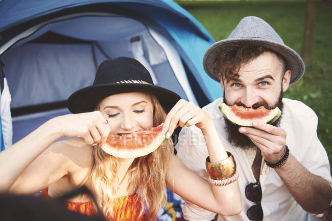 Giovane coppia in trilbies fare faccina sorridente con fetta di melone al festival — Foto stock
