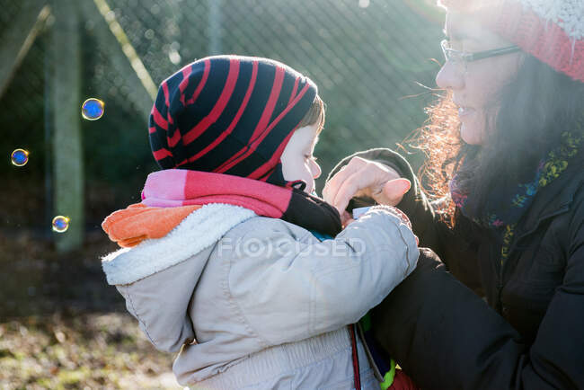 Masculino criança e mãe soprando bolhas no parque — Fotografia de Stock