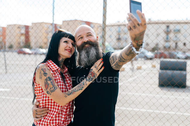 Mature hipster couple taking selfie by wire fence — Stock Photo