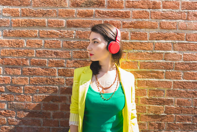 Молода жінка в навушниках біля цегляної стіни — стокове фото