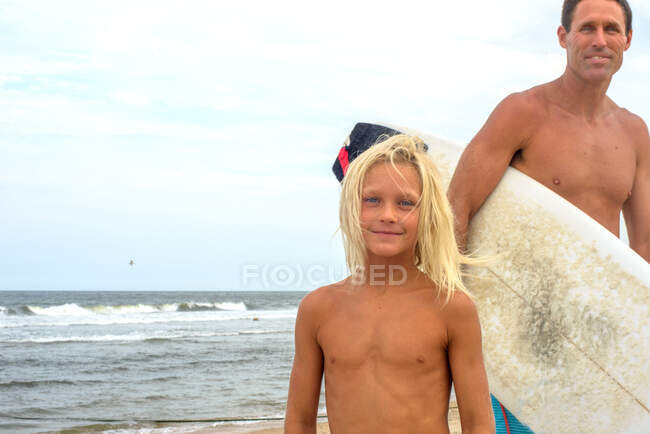 Retrato de surfista varón maduro e hijo rubio en la playa, Asbury Park, Nueva Jersey, EE.UU. - foto de stock