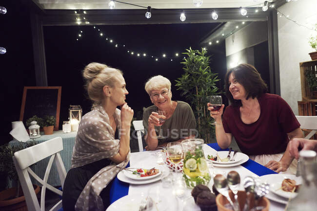 Three women sitting at dinner table, drinking from wine glasses — Stock Photo